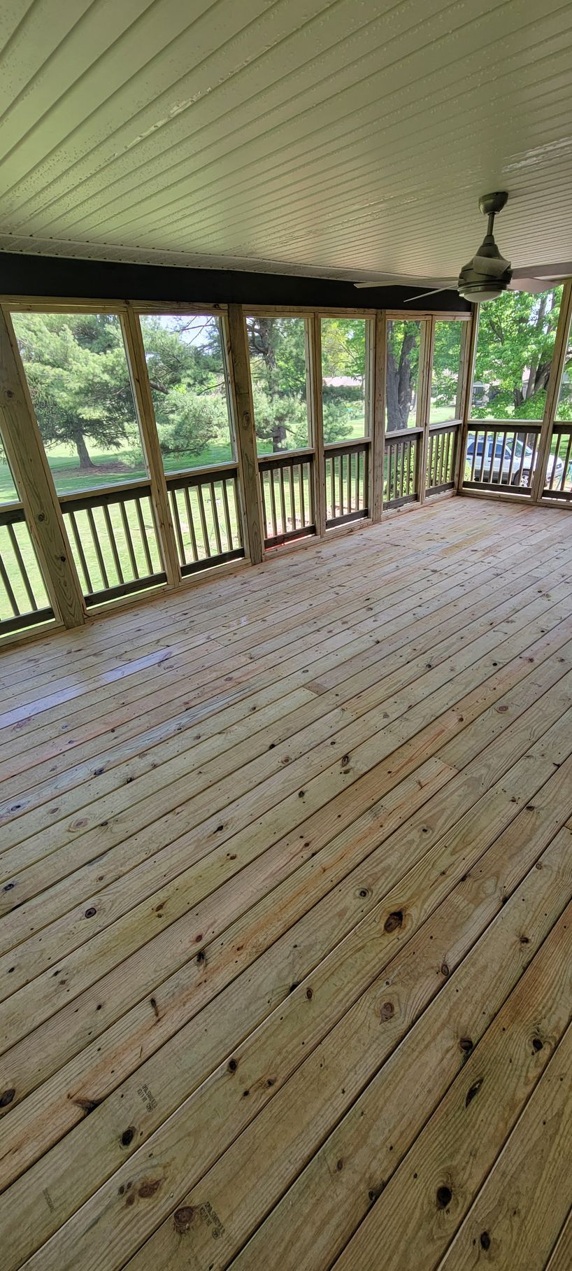 A screened in porch with a wooden floor and a ceiling fan.