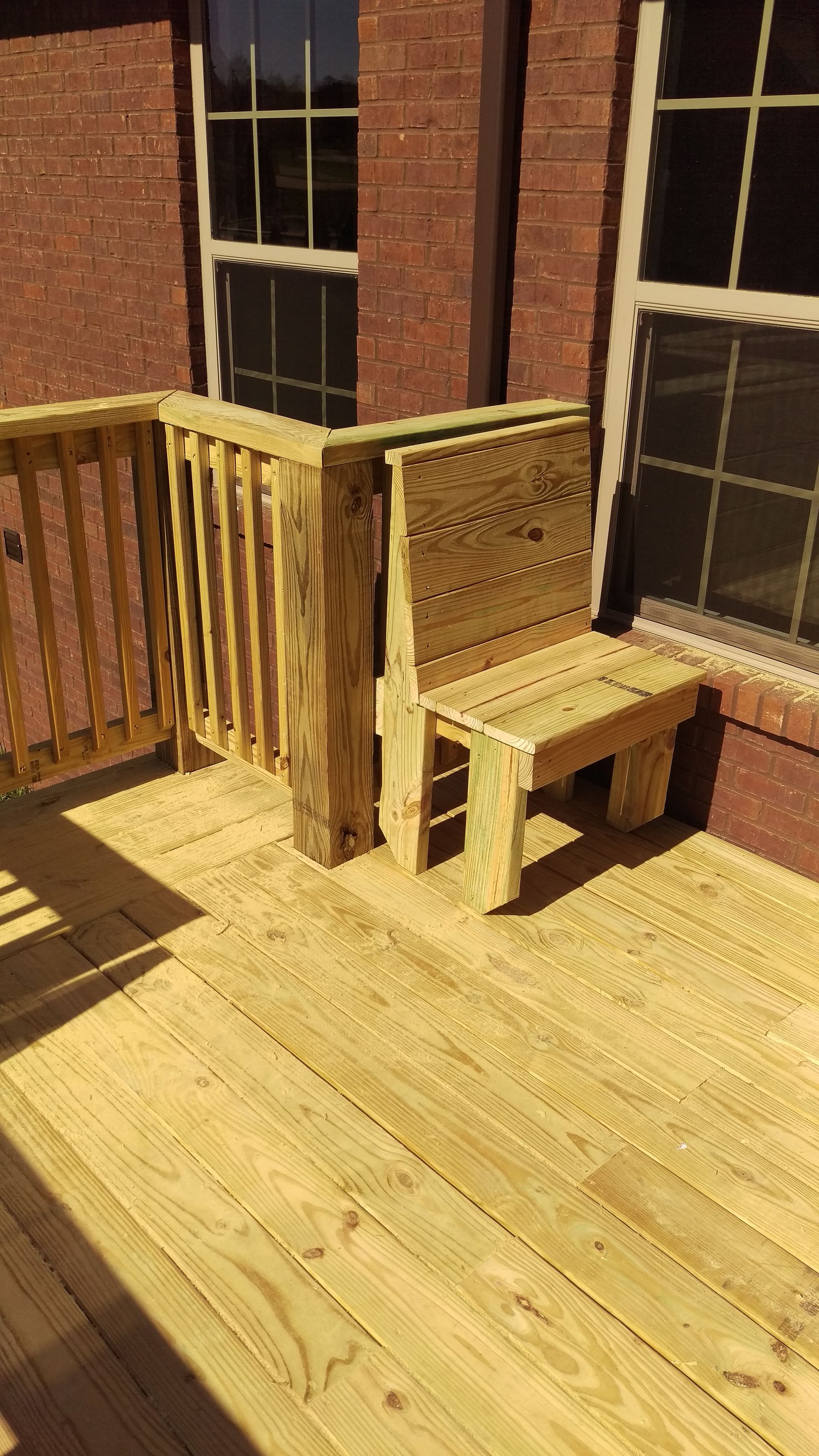 A wooden deck with a chair and a bench in front of a brick building.