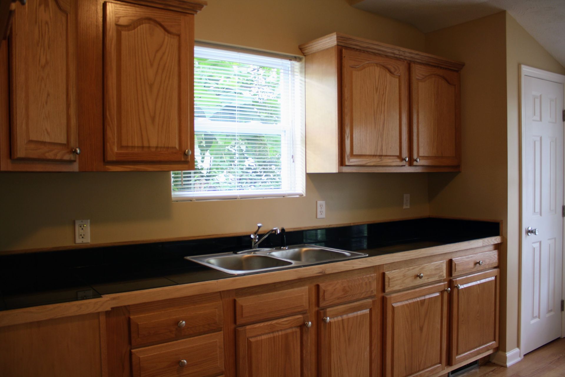 An empty kitchen with wooden cabinets , a sink , and a window.
