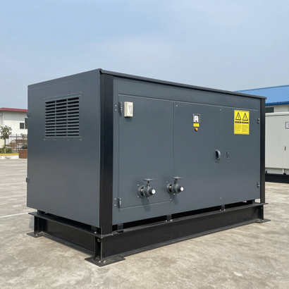 Gray industrial generator enclosure on a concrete pad outdoors, with vents, warning labels, and metal fittings