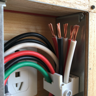 Loose electrical wires inside a wooden cabinet beside a wall outlet