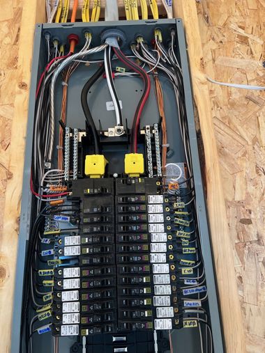 Open electrical breaker panel with rows of circuit breakers and bundled wiring in a wooden wall cavity