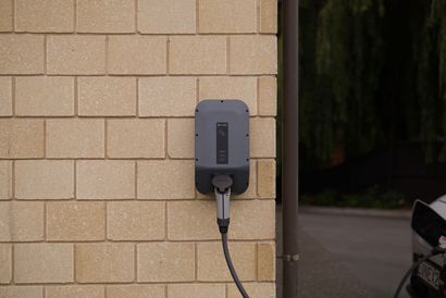 Wall-mounted EV charging station on a beige brick exterior wall with a cable plugged in.
