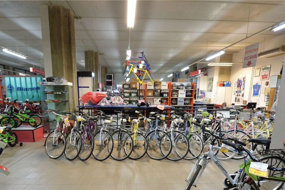 Interno di un negozio di biciclette con file di bici, scaffali di accessori e telai di bici appesi.