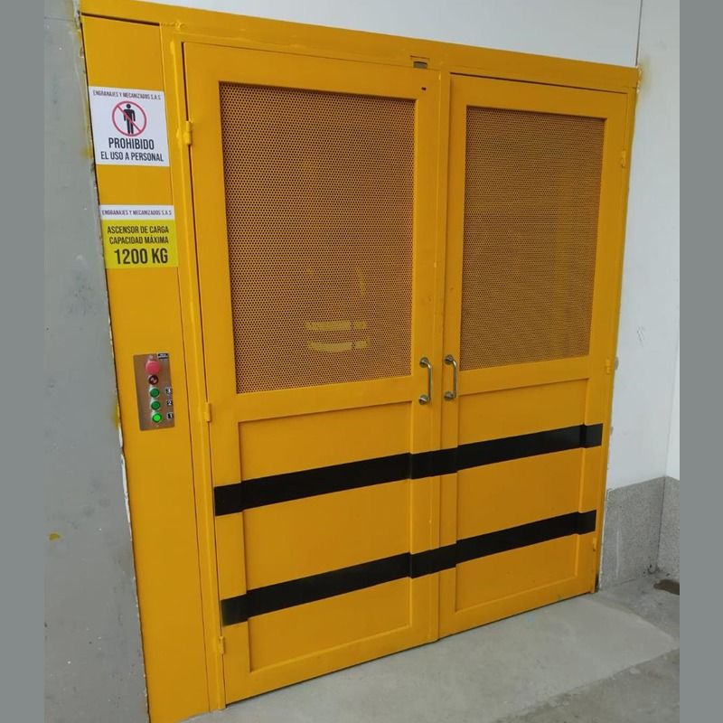 Montacargas industrial amarillo con puertas de malla y franjas negras de seguridad en un pasillo