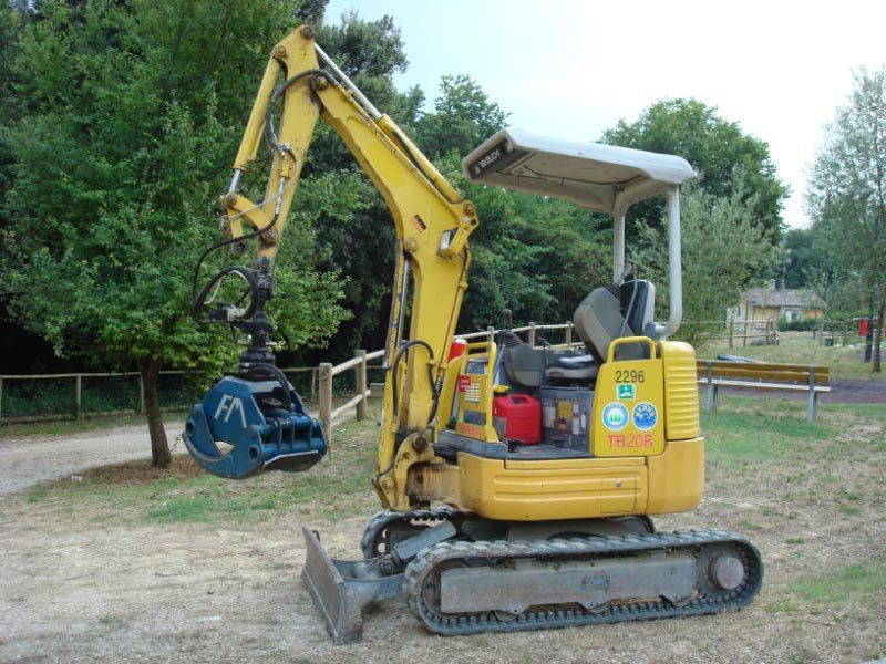 Un escavatore giallo è parcheggiato in un campo con alberi sullo sfondo