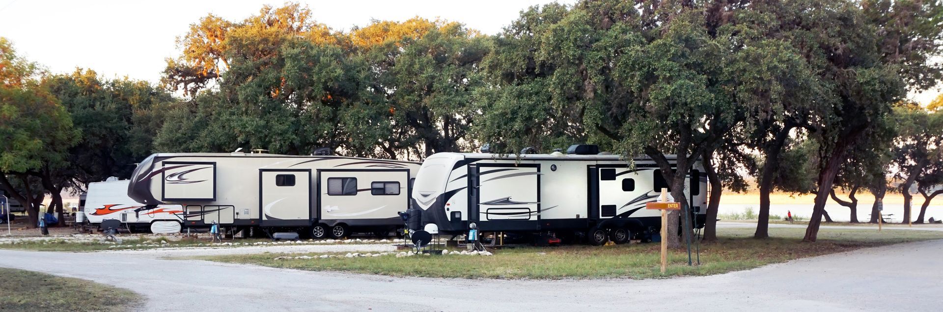 a row of rvs are parked in a park surrounded by trees .