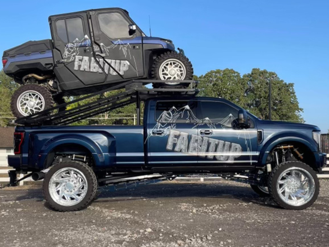 Dark blue lifted truck with a utility vehicle on a custom rack on top. 