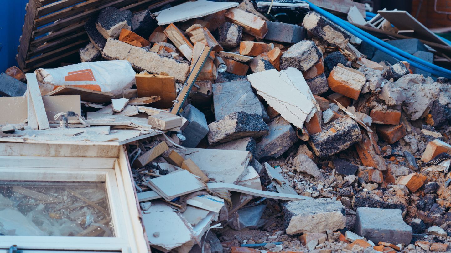 Pile of demolition debris, including bricks, concrete, and wood, with a window frame in the foreground.