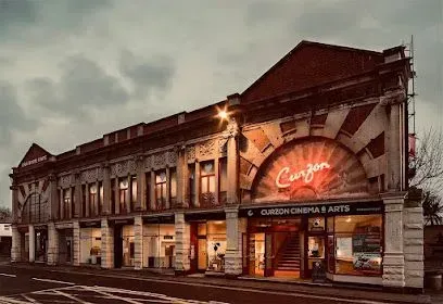 Historic Curzon Cinema & Arts building with arched entrance and neon sign, under cloudy sky.