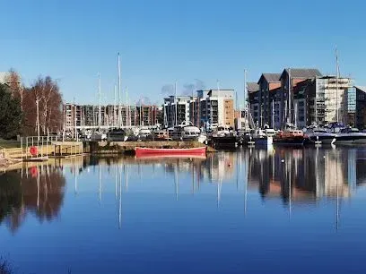 Harbor with boats and modern buildings under a clear blue sky. Water reflects the buildings and boats.