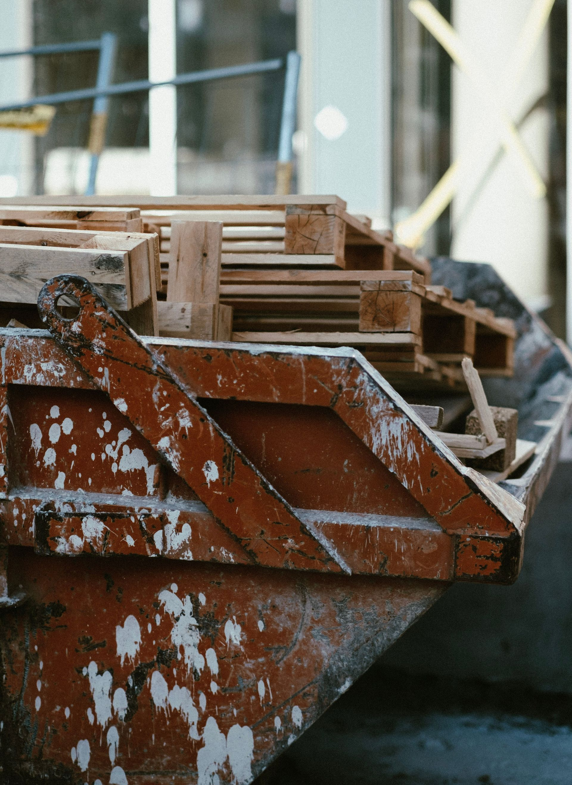 Rusty construction dumpster filled with wooden debris, with white paint peeling on the side