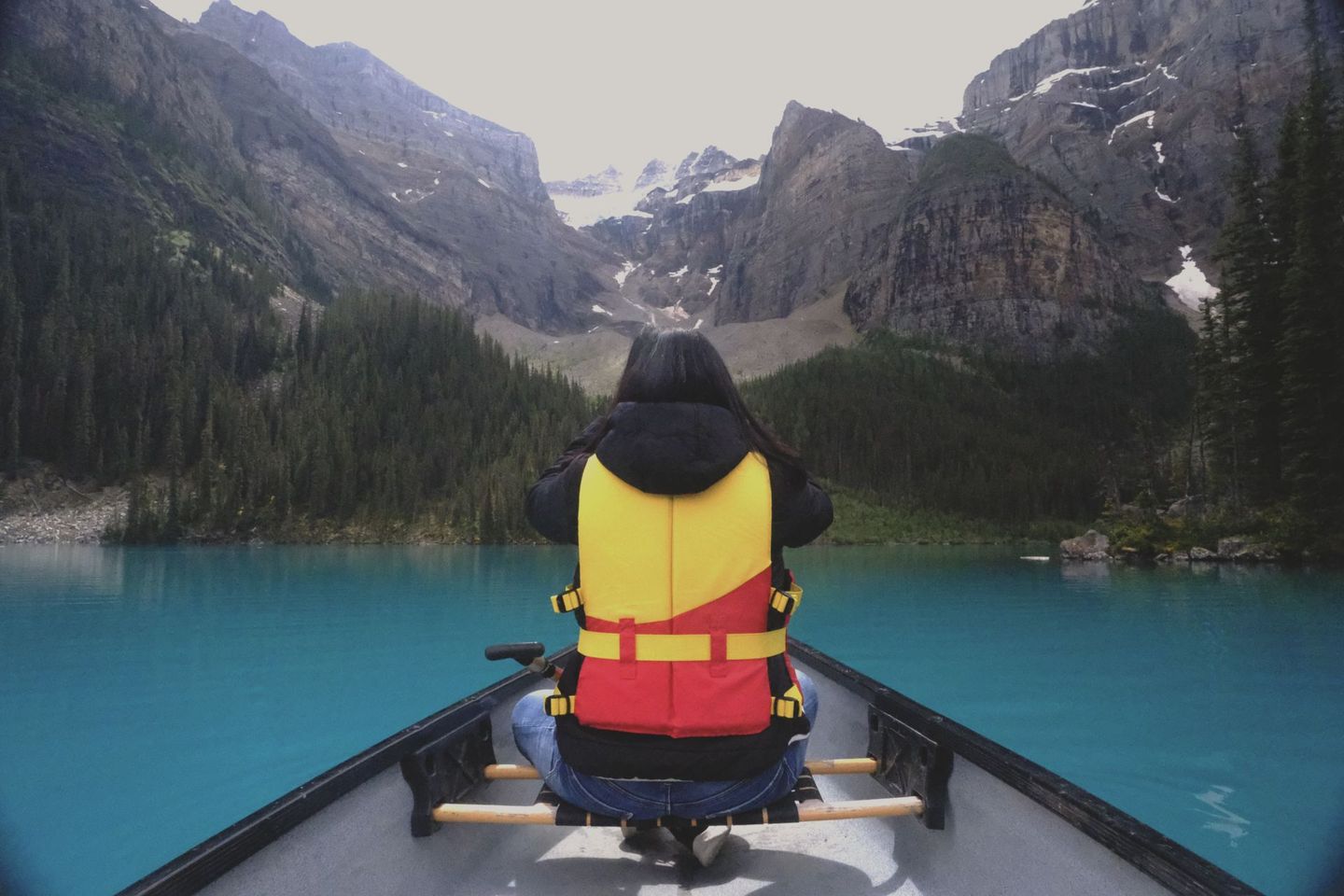 Guest canoeing on turquoise Moraine Lake with mountain peaks reflection, Banff Bear Travel optional canoe experience