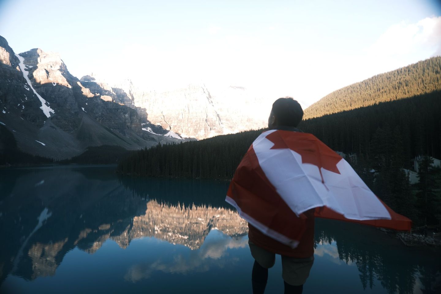 Guest wrapped in Canadian flag at Moraine Lake at dawn with perfect mountain reflections, Banff Bear Travel tour