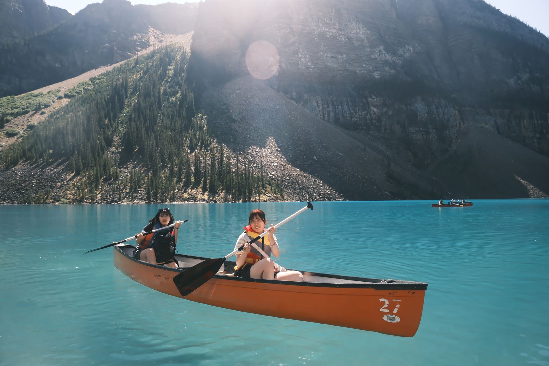 Candid professional photo of two friends canoeing at Moraine Lake, illustrating the slow travel philosophy and unhurried pace of Banff Bear Travel’s sunrise expeditions.