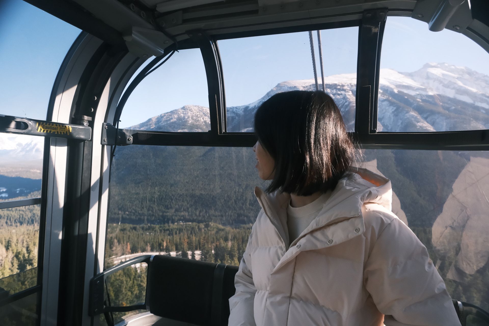 A solo female traveler capturing the stunning 360-degree panoramic views of the Canadian Rockies from the Banff Gondola summit, featuring professional photography guidance by Banff Bear Travel.