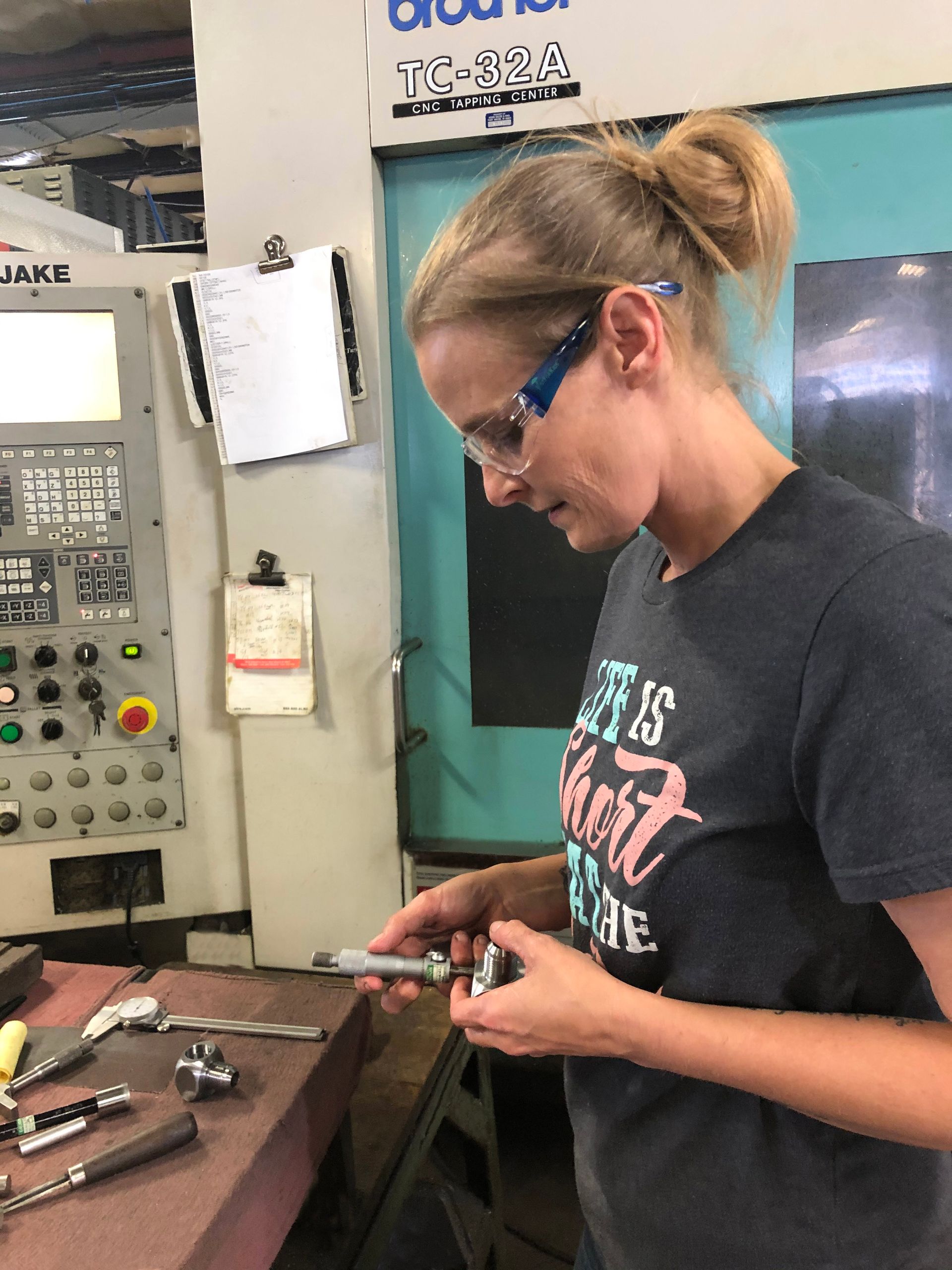 A woman wearing glasses is working on a machine in a factory.