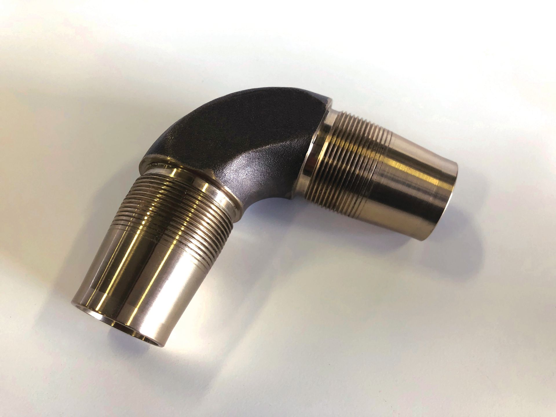 A close up of a metal elbow on a white surface