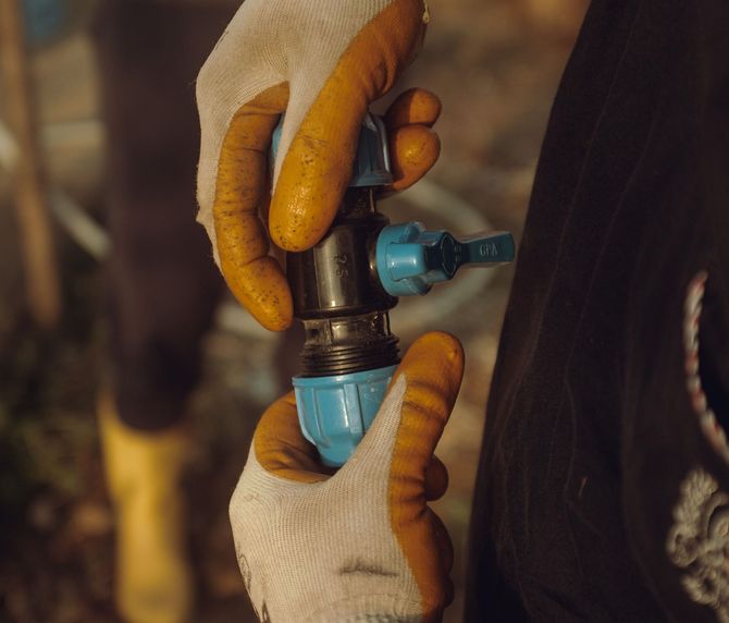 Gloved hands adjust a blue plastic valve on a black pipe.