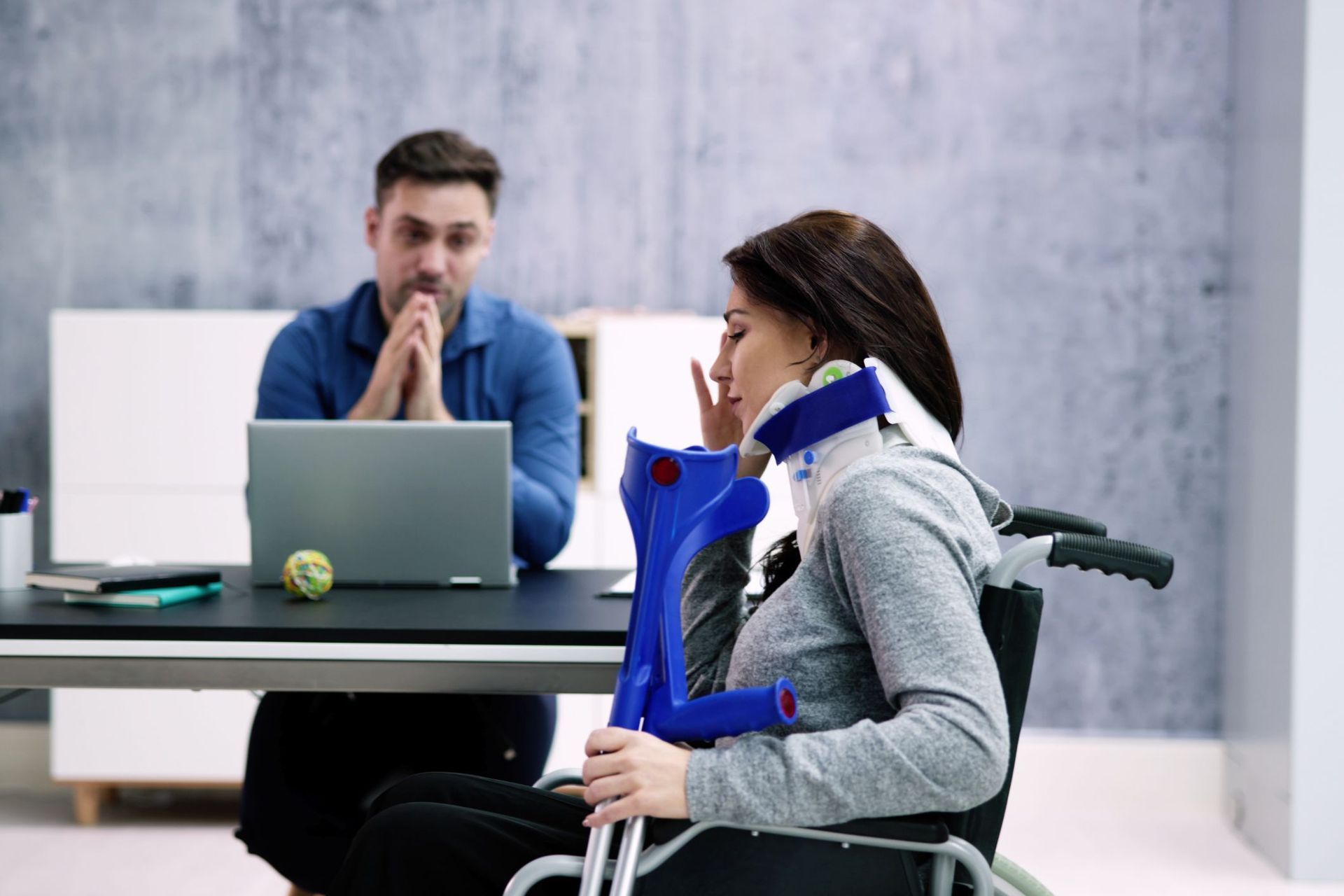 A woman in a wheelchair is talking to a man in front of a laptop.