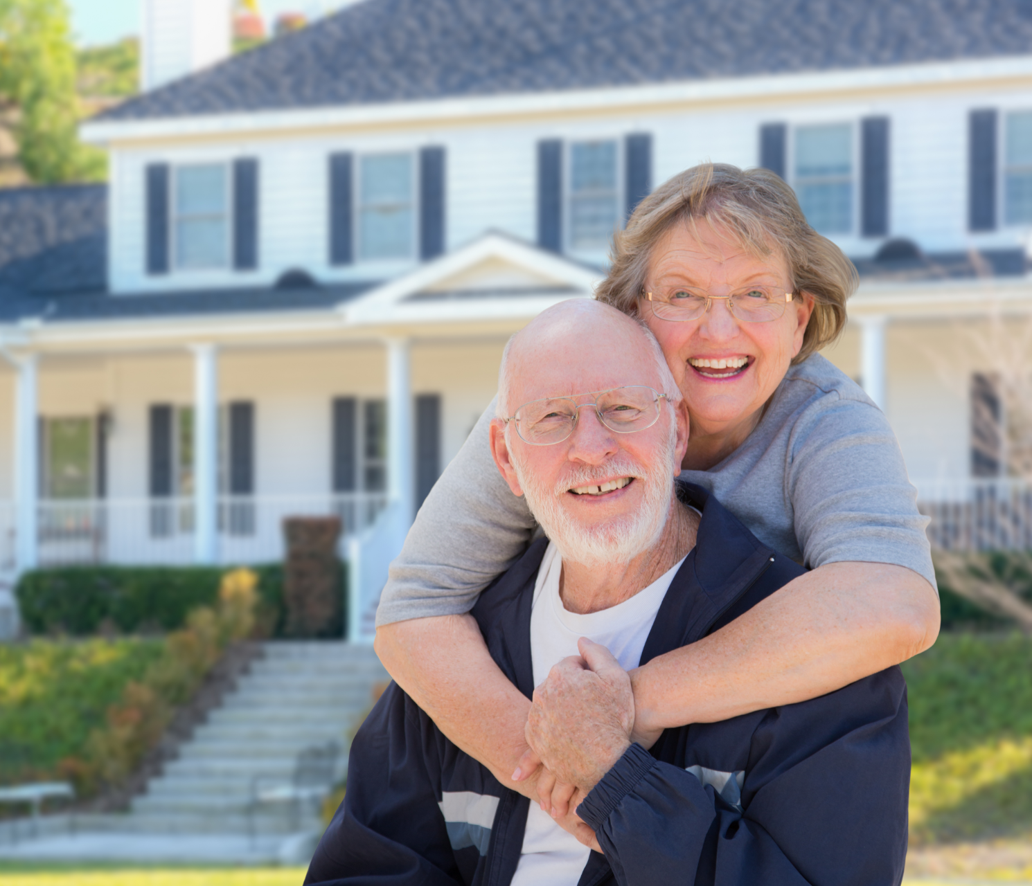 A woman is giving an older man a piggyback ride in front of a house.