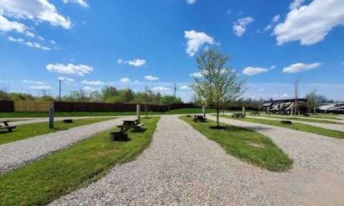 a gravel path leading to a park with picnic tables and trees .
