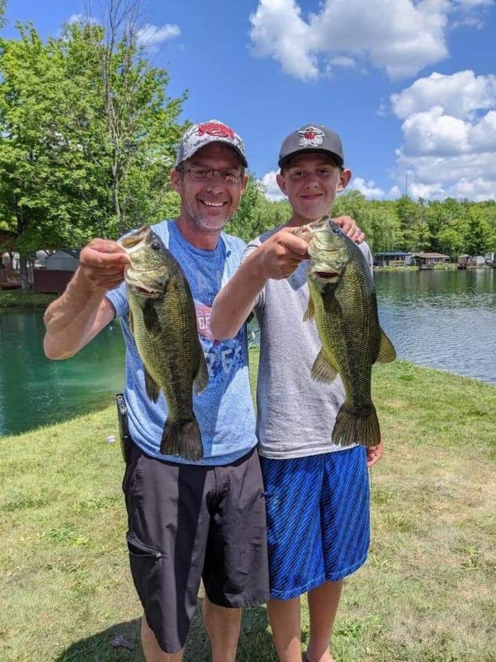 a man and a boy are holding two bass in front of a lake .