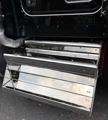 Chrome step plates on the side of a black semi-truck, reflecting the surrounding environment.