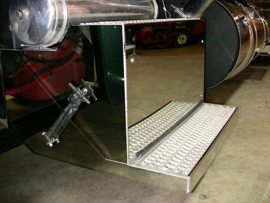 Polished metal truck step with diamond plate treads. Attached to a large chrome exhaust component.