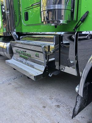Bright green semi-truck with chrome steps and trim, parked outdoors on concrete.