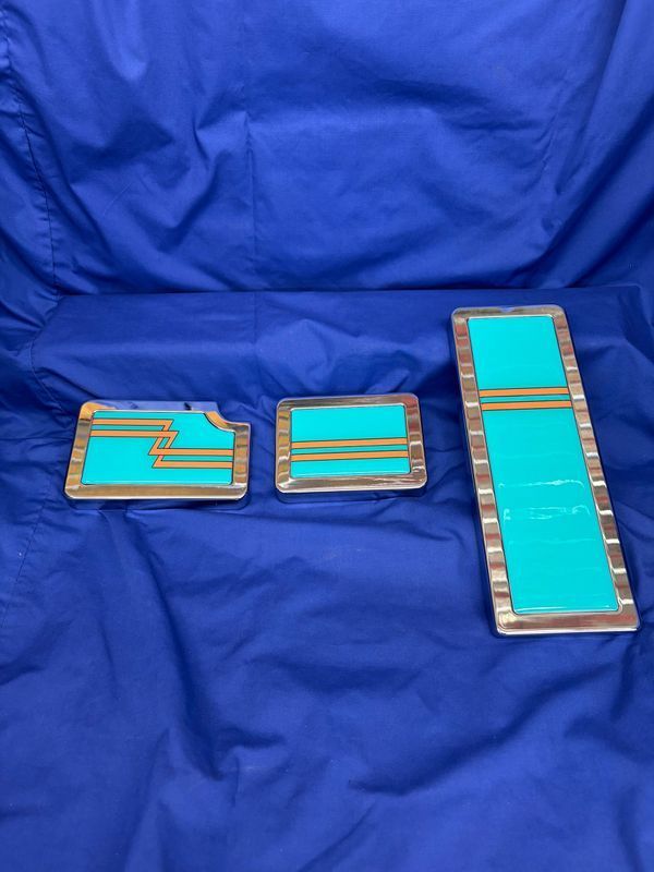 Three rectangular turquoise and gold metal art pieces on blue fabric.