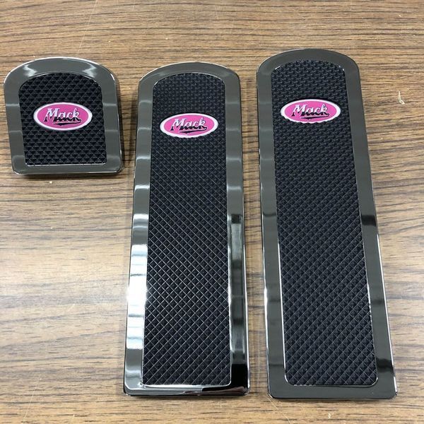Set of three Mack truck pedal covers with chrome trim and pink logo on black textured surface.