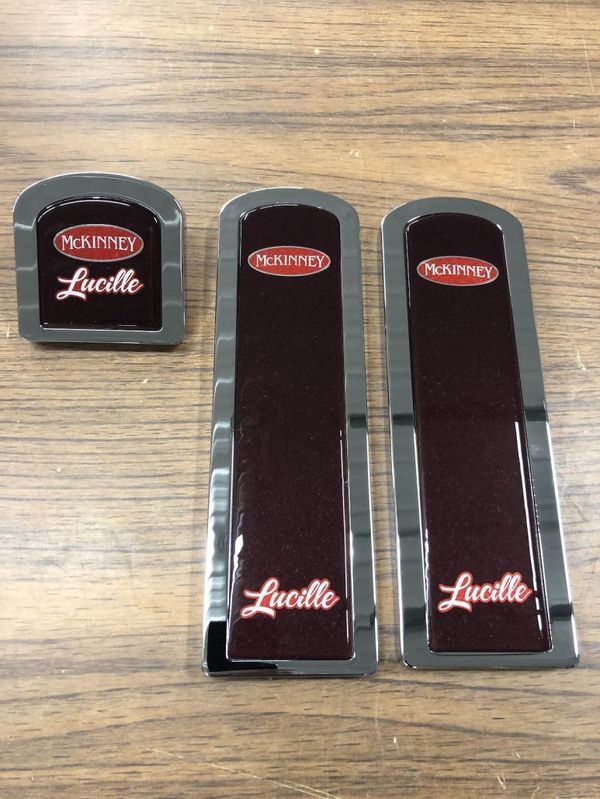 Three maroon and silver truck emblems on a wooden surface, labeled
