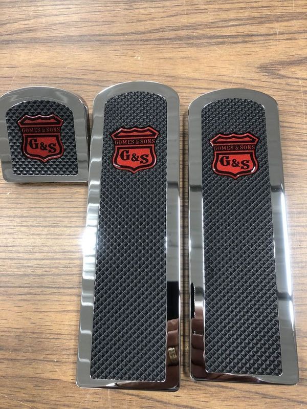 Chrome G&S logo foot pedals on a wood surface. Black textured centers, red logos.