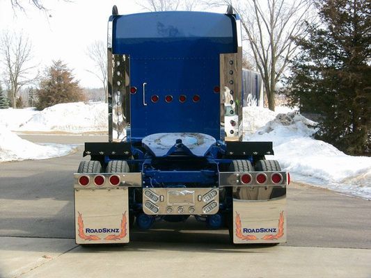 Blue semi-truck rear view with mud flaps. Snow on the ground in background.