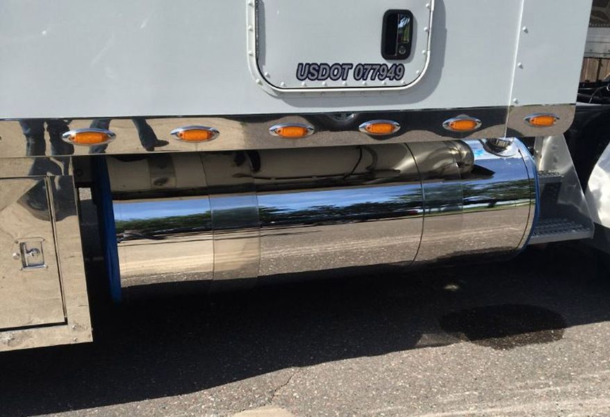 Chrome fuel tank and trim on a semi-truck with amber lights, parked outdoors.