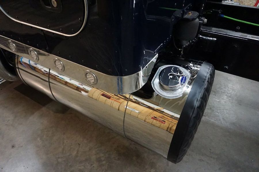 Chrome fuel tank on a semi-truck with a black cap, reflecting the setting.