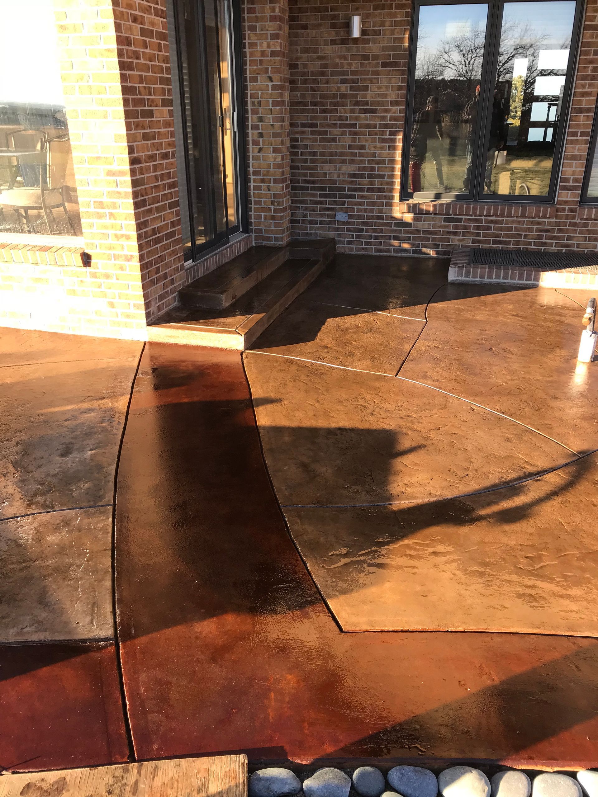 Outdoor concrete patio with brown and reddish-brown stained finish near a brick building.
