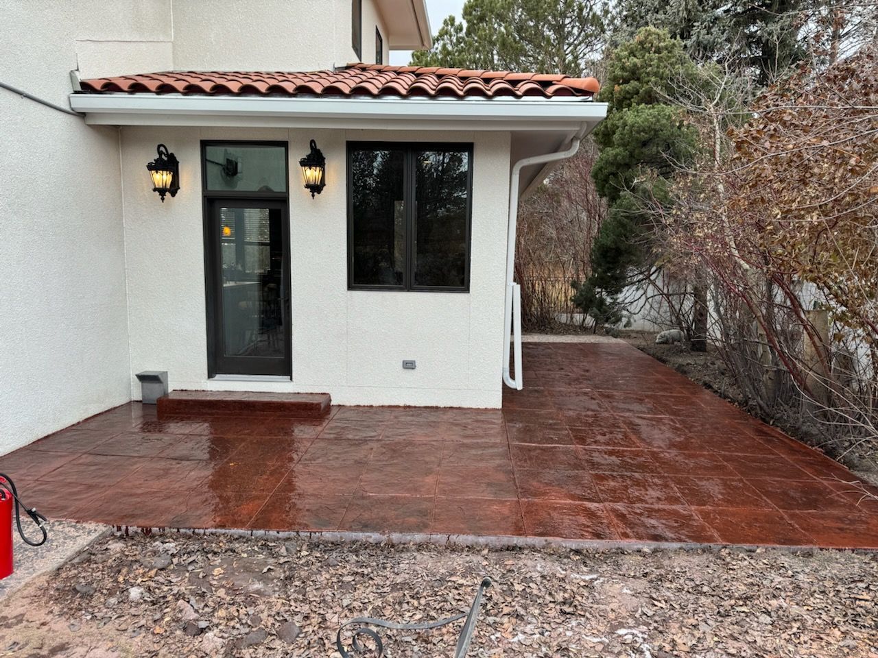 Red brick patio outside a white building with black windows and a door.