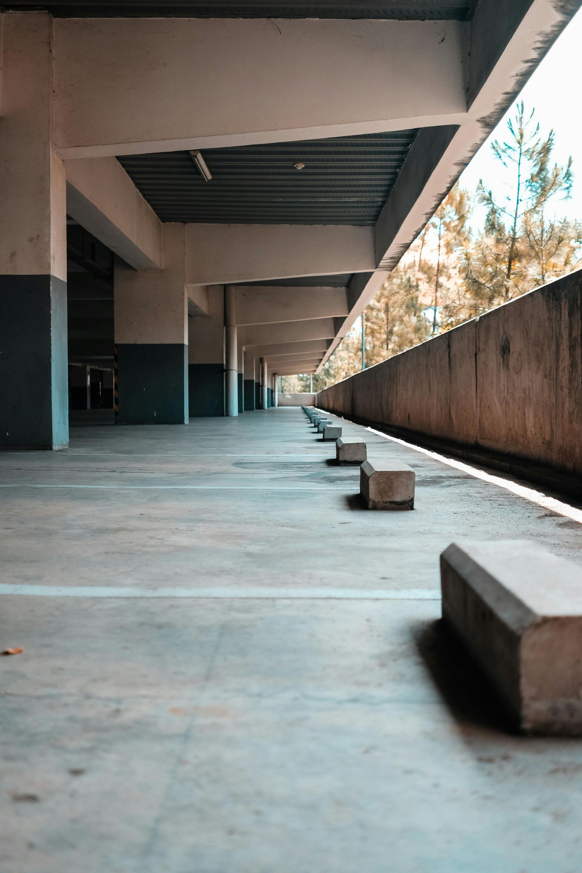Empty parking deck with concrete pillars, parking stops, and a view of trees through an open wall.