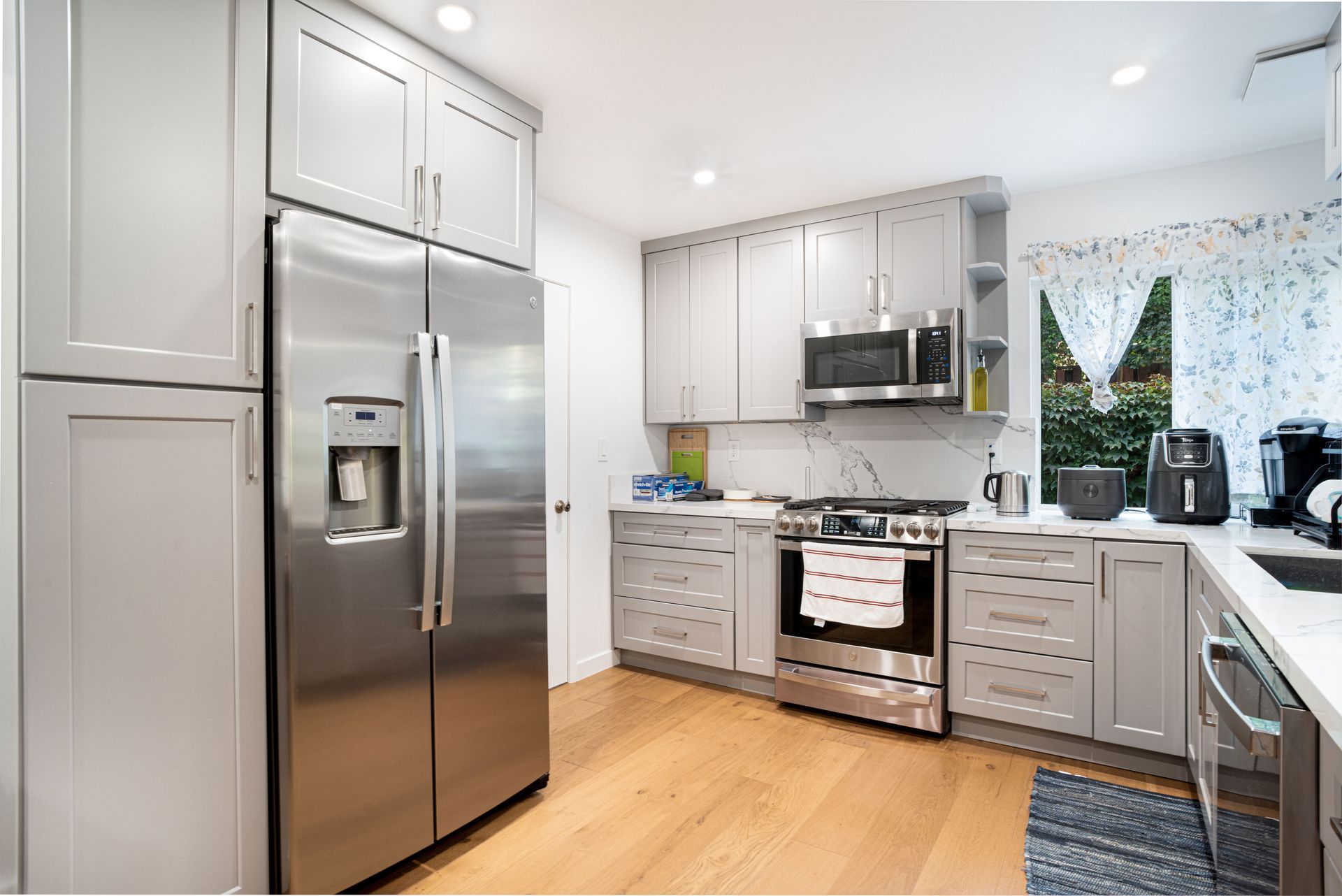 Bright modern kitchen with stainless steel appliances, white cabinets, and wood floors