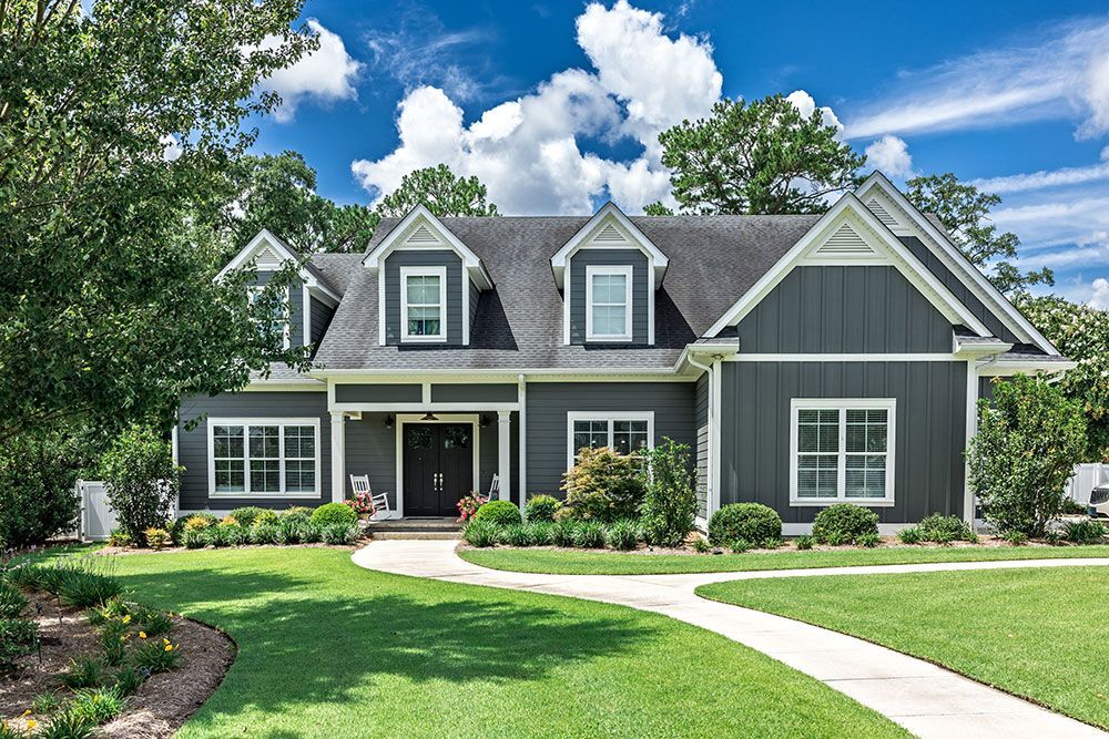 Gray house with white trim, green lawn, blue sky, and a winding walkway.