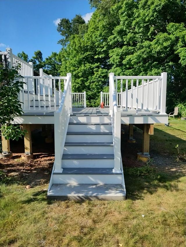 White-railed deck with gray steps leading to a raised platform on wooden supports, set in a grassy yard.