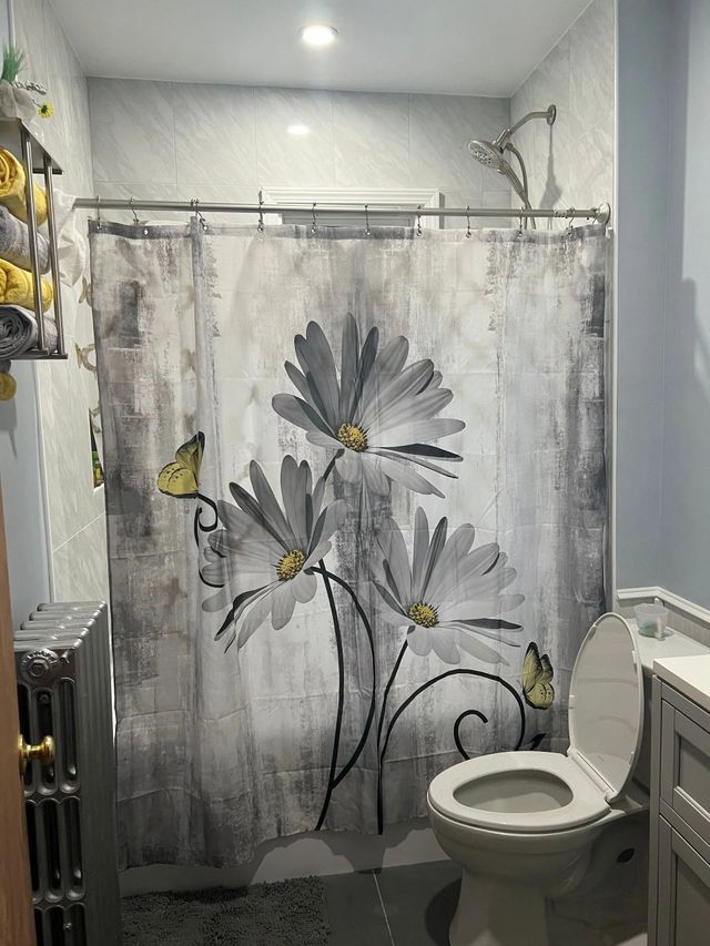 Bathroom with floral shower curtain, toilet, and light blue walls.