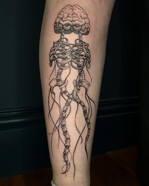 A black and white tattoo of a jellyfish with brains and skeletons
