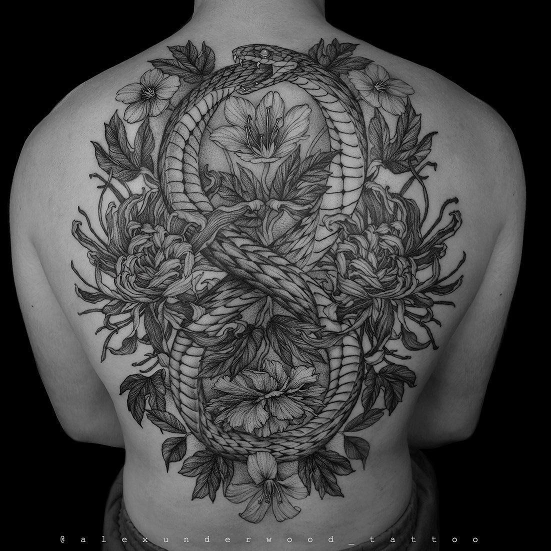 A man has a tattoo on his back of a snake and flowers.