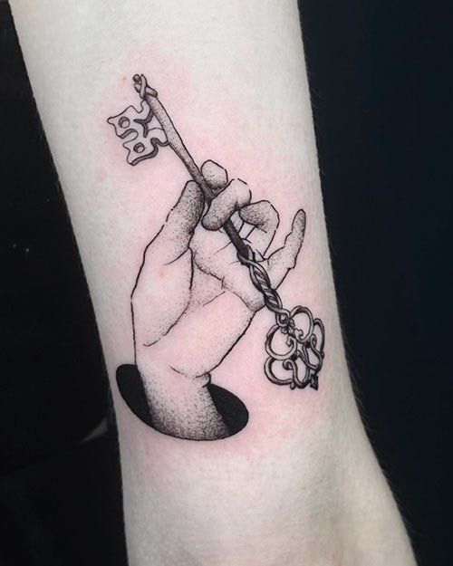 A black and white tattoo of a hand holding a key