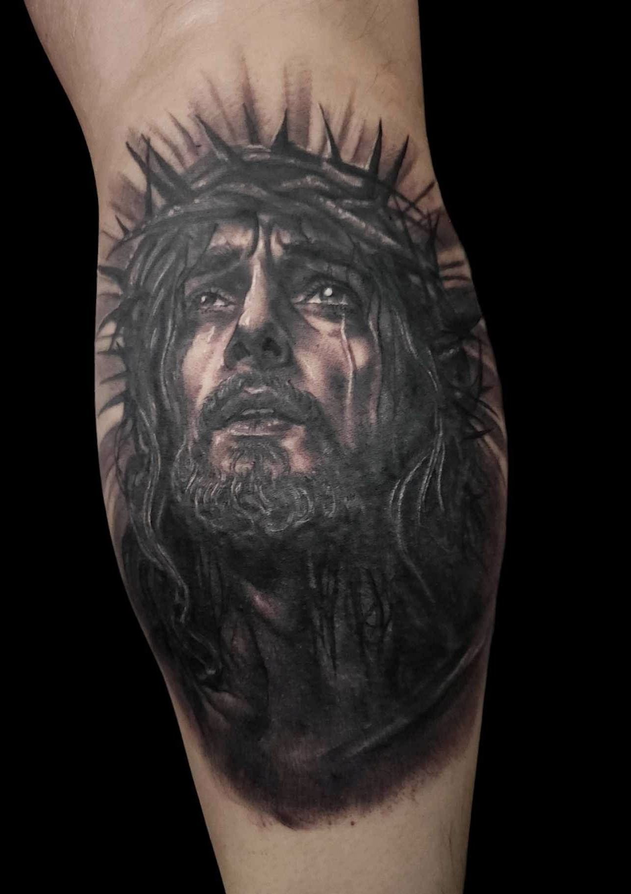 Black and gray tattoo of a crowned, tear-streaked face on skin, with a dark smoky background