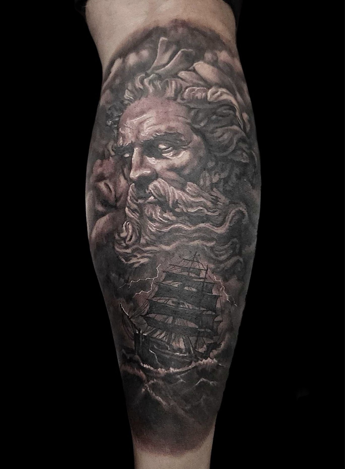 Dark grayscale tattoo of a bearded classical face on a forearm, with ornate details and shading