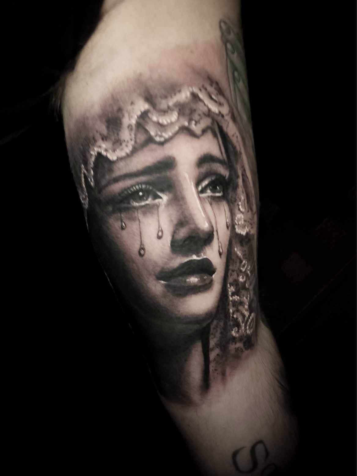 Black-and-gray tattoo of a crying face on an arm